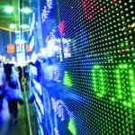 A large display of stock prices on the side of a building.